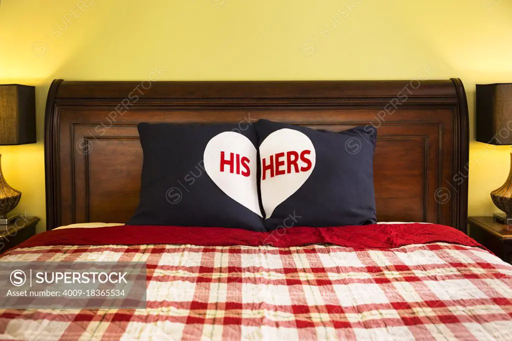 Detail shot of decorative His and Hers Pillows on dark wooden sleigh bed with red and white plaid comforter in master bedroom of home 