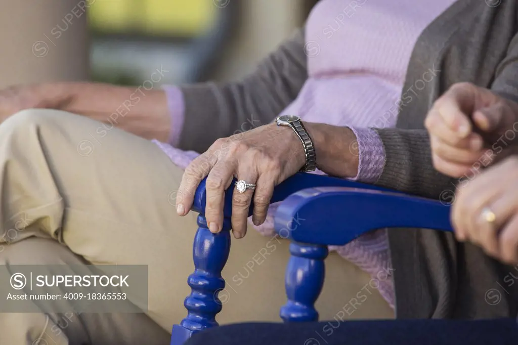 Older couple sitting in rocking chairs, detail on womans hand with ring resting on chair