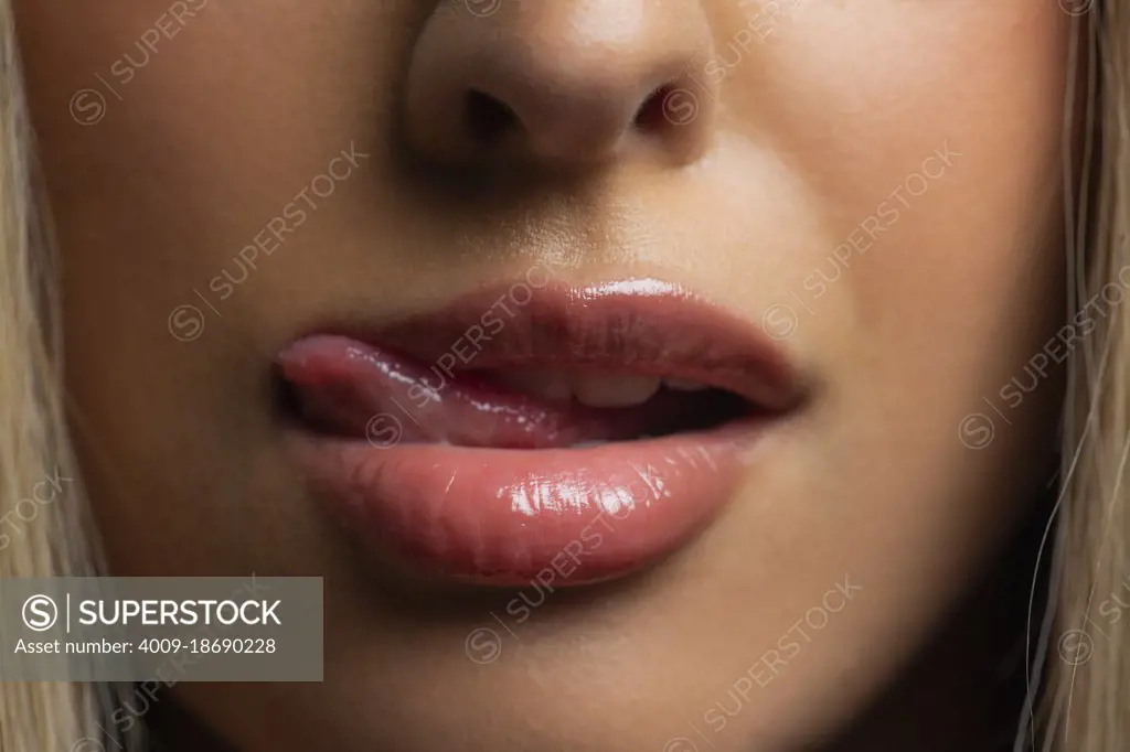 Close up portrait of Hispanic womans mouth licking lips, with glossy  lipstick. - SuperStock