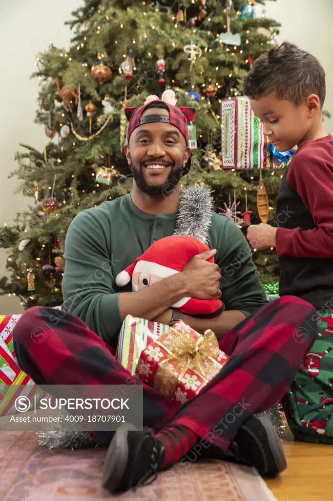 Proud father sitting in front of Christmas tree with family. 