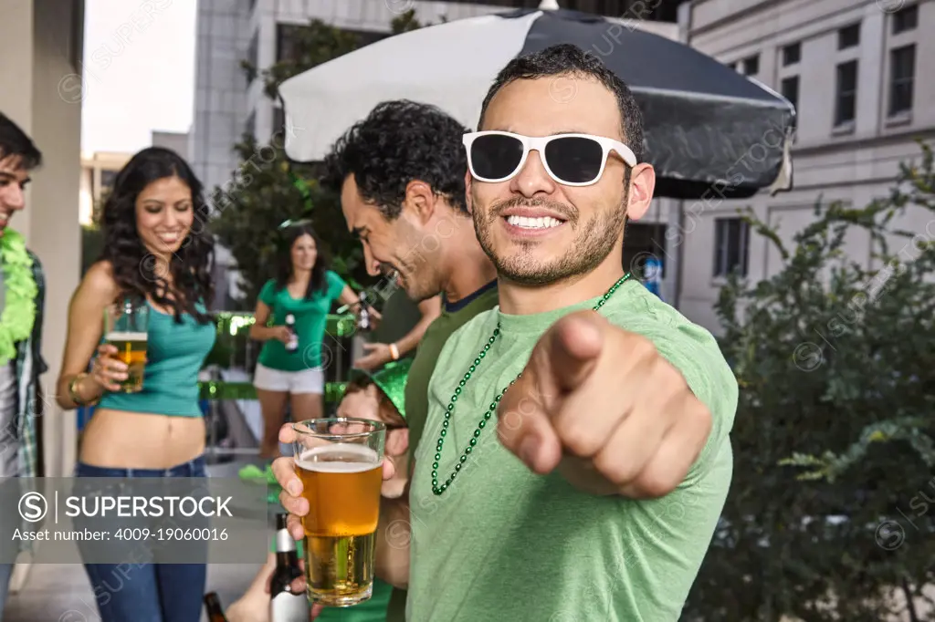 Portrait of a man pointing at camera while holding a beer glass at party for St Patrick's Day.