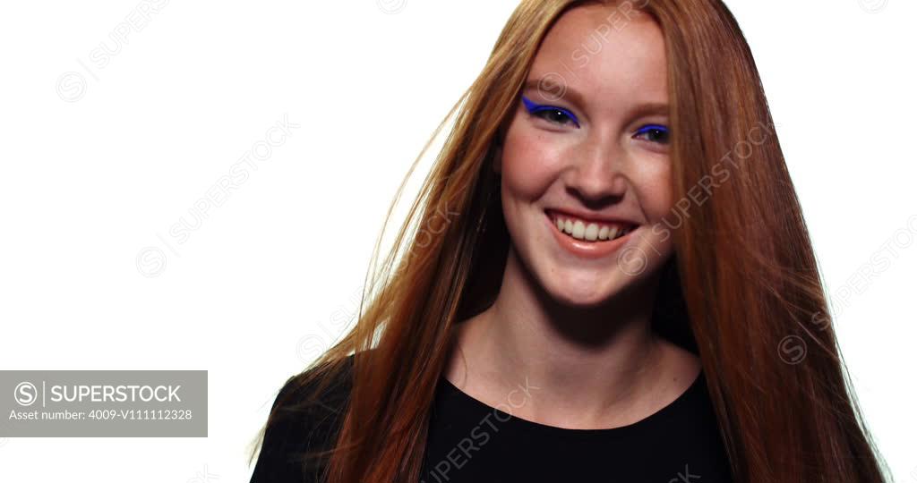 Portrait of a redhead teen looking into camera and smiling while her hair blows in the wind. - SuperStock