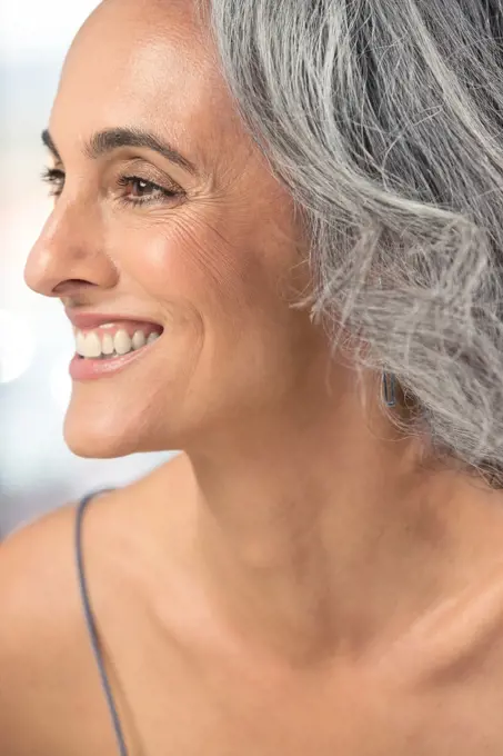 Close up profile of a youthful middle-aged woman with gray hair, smiling.