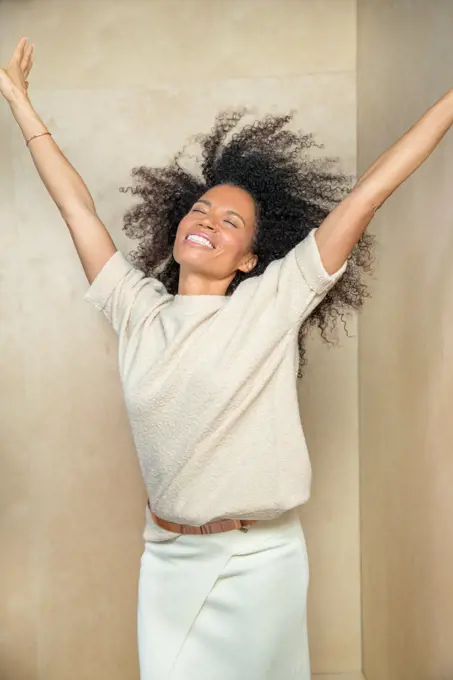 A middle-aged woman with her hands in air and head tilted back laughing.