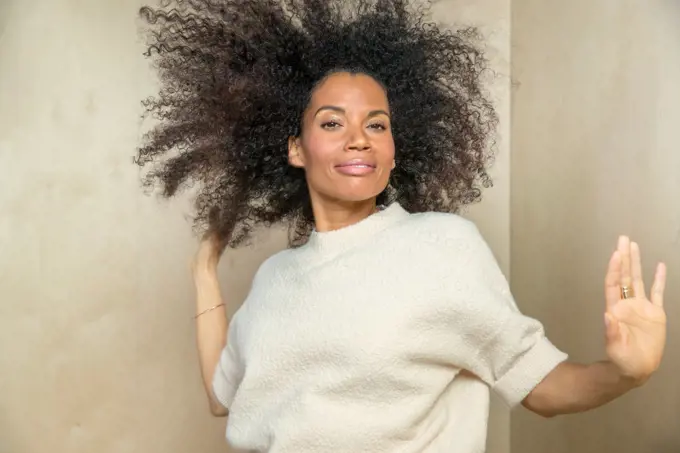 A mixed race , middle-aged woman dancing with her hands out towards camera.