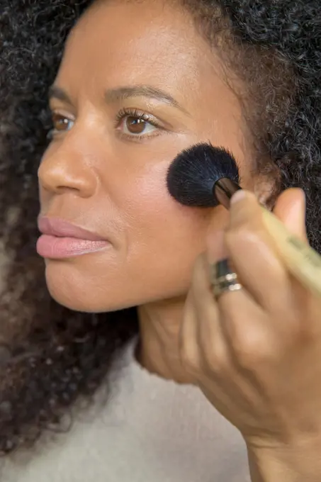 Mixed race, middle-aged woman looks off camera while putting on make up.