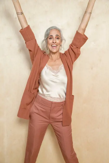 A middle-aged woman with grey hair smiling with her hands up.