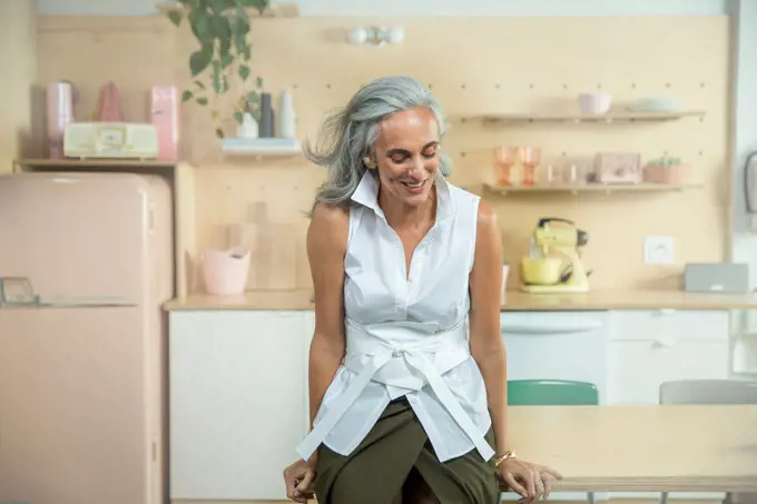 Youthful middle-aged woman, with gray hair leaning on a kitchen table looking down off camera.