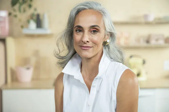 Close up portrait of a middle-aged woman with natural gray hair looking into camera with a warm smile.