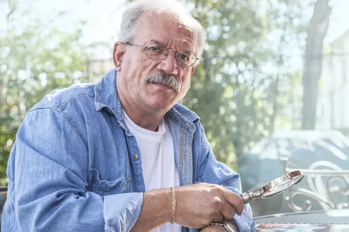 Serious older man holding magnifying glass