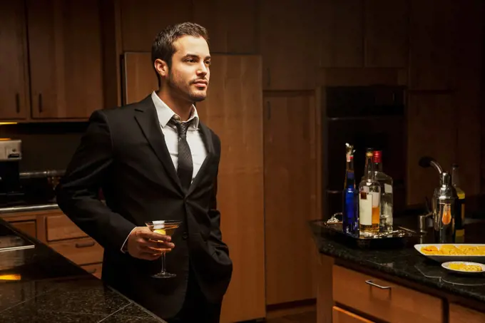 Hispanic man drinking martini in kitchen