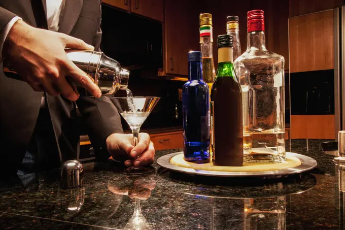 Hispanic man pouring martini in kitchen