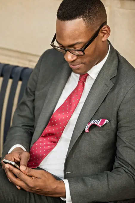 Black businessman using cell phone on bench