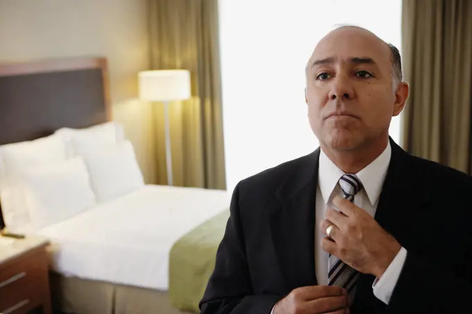 Middle-aged businessman adjusting tie in hotel room