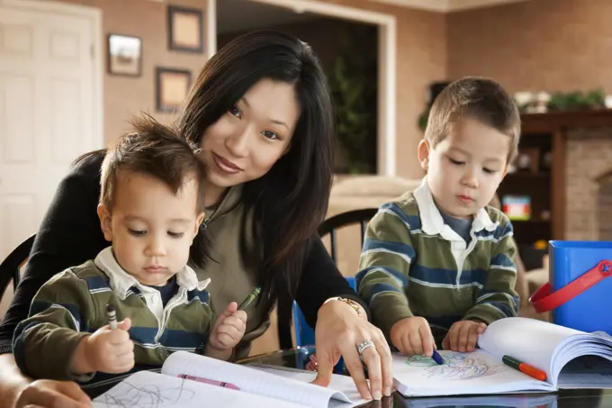 Asian mother watching sons draw with crayons