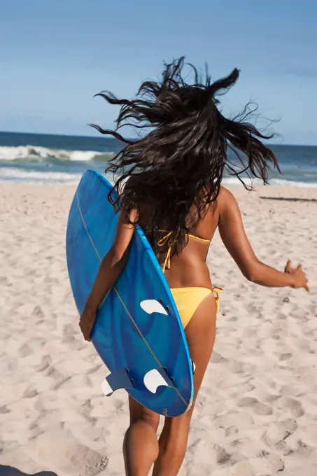 Mixed race woman running with surfboard on beach