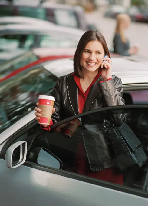 Woman getting into car holding coffee and cell phone