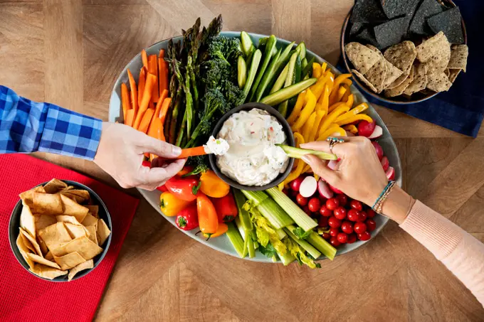 Two people dipping appetizers into a veggie dip.