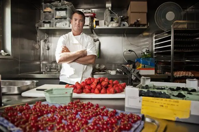 Pastry chef with his arms crossed standing in a kitchen with assorted berries being prepped on counter