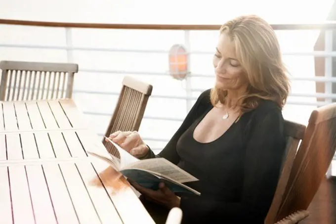 Ecuador, Galapagos Islands, Woman reading magazine while sitting at table on deck of cruise ship