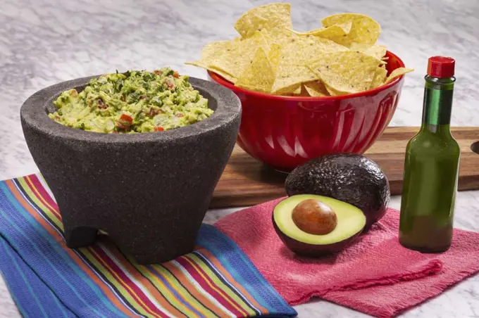 Guacamole and Chips with green hot sauce and a molcajete