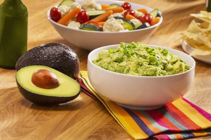 Guacamole and Chips with a green hot sauce and veggies. 