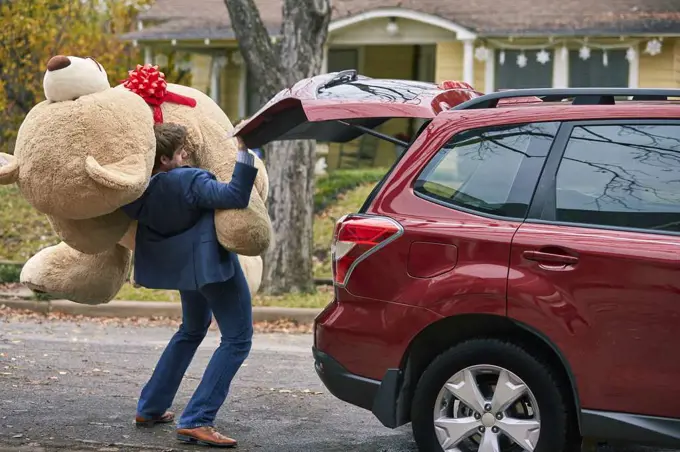 A goofy young man struggling to pull out an oversized teddy bear, stumbling over himself.