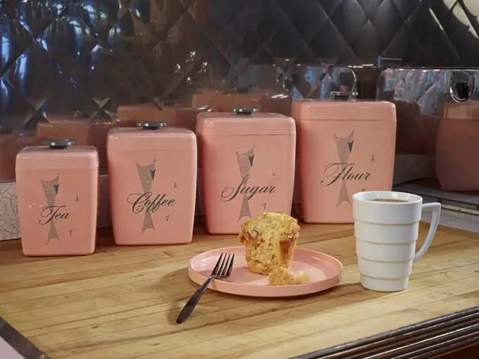 Coffee and muffin on countertop in front of vintage, kitchen canisters. 