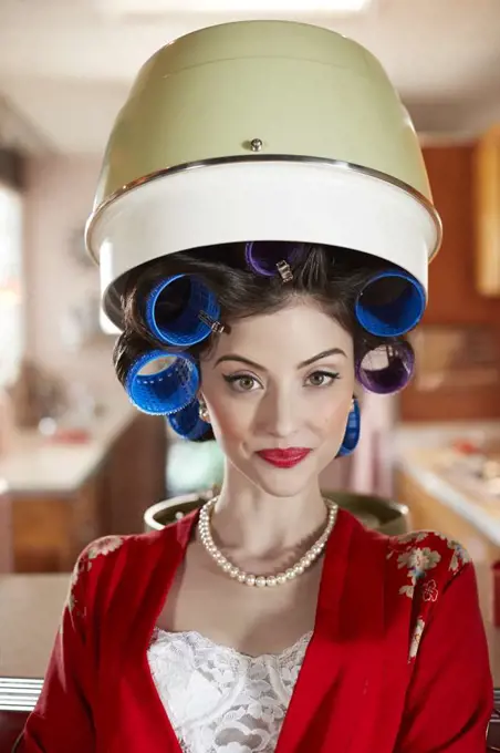 Portrait of contemporary woman sitting under a vintage hair dryer in a mid-century modern environment.