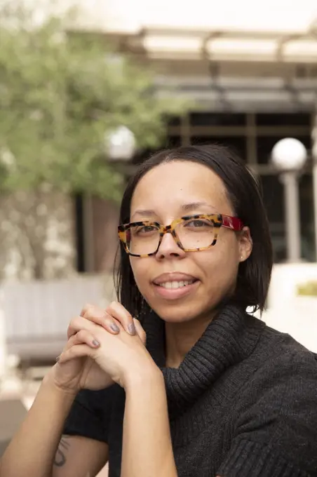 portrait of young ethnic woman with long black hair  and glasses sitting in park looking towards camera 