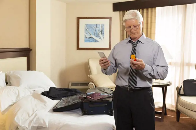 Mature Caucasian man in a hotel room, using cell phone to check prescription medication