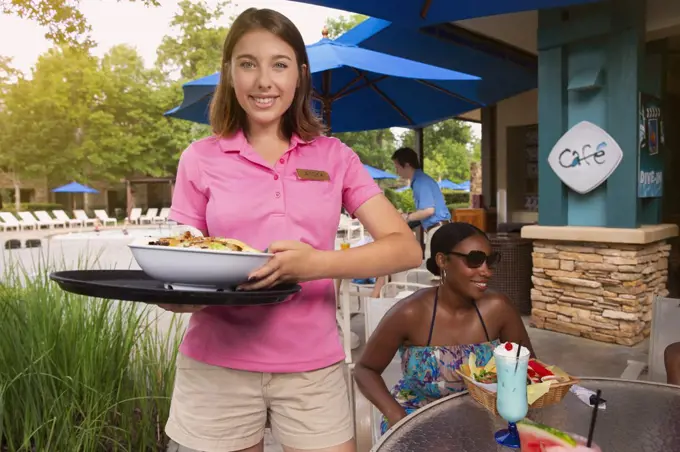 Portrait of a female waitress delivering salad to guest at poolside Hotel Cafe