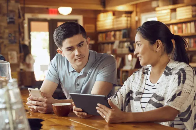 Young man and woman sitting at counter in cafe bookstore looking at tablet 