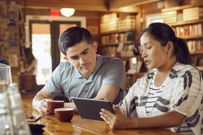 Young man and woman sitting at counter in cafe bookstore looking at tablet 