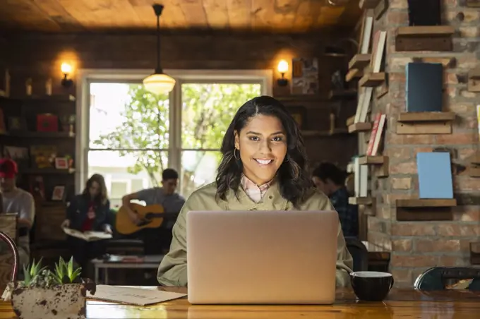 Portrait of young woman sitting at table in coffee shop bookstore using laptop computer 