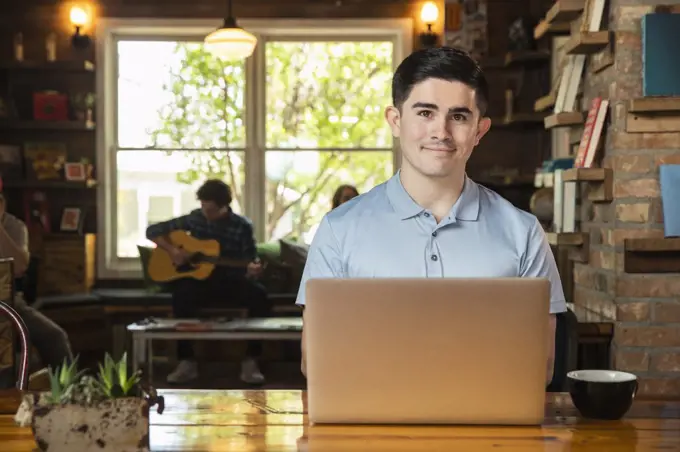 Portrait of young man sitting at table in coffee shop bookstore using laptop computer 