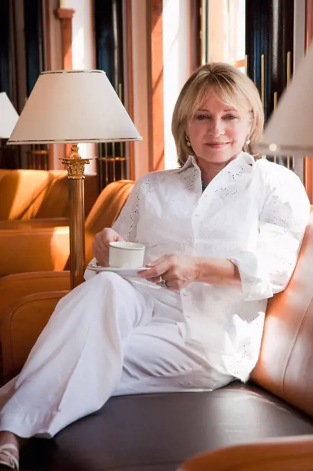 Mature woman drinking coffee while sitting on a leather couch in a ship lounge