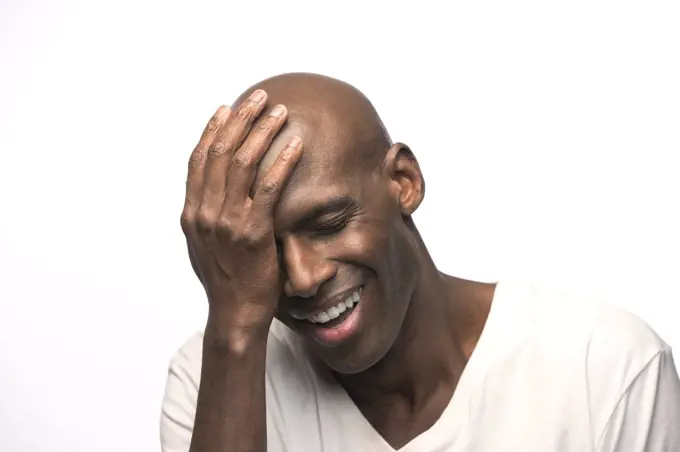 Portrait of young bald African American man with hand on his head looking down with eyes closed 