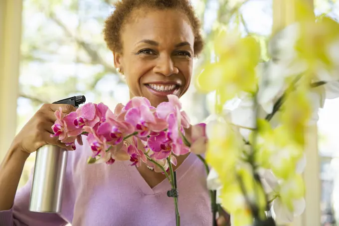 Older  woman watering orchid flowers with spray bottle on porch of home 