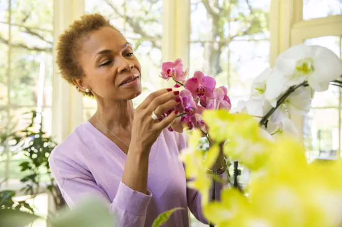 Older  woman watering orchid flowers with spray bottle on porch of home 