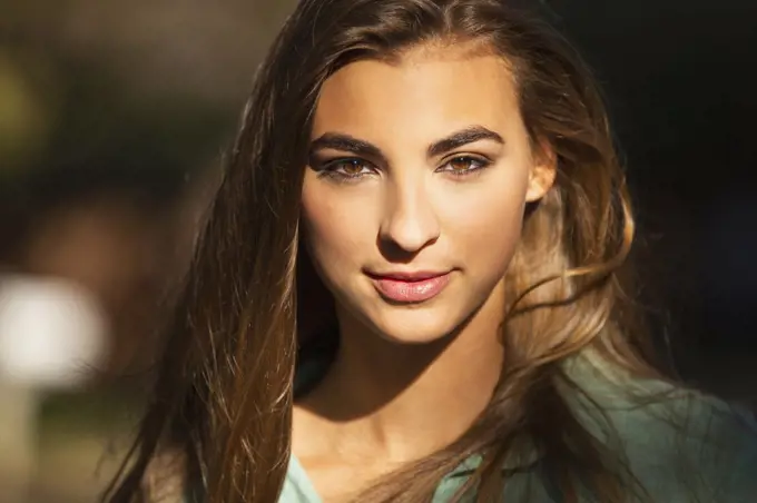 Portrait of young woman standing outside in bright sun, looking into camera lens 