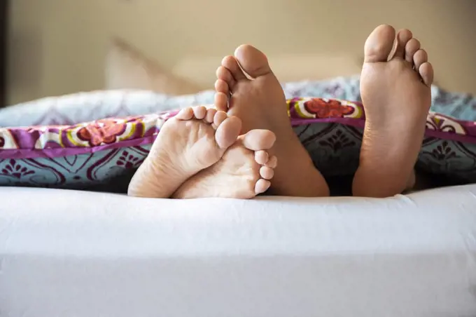 Close-up of bare feet sticking out from covers while couple lays in bed 