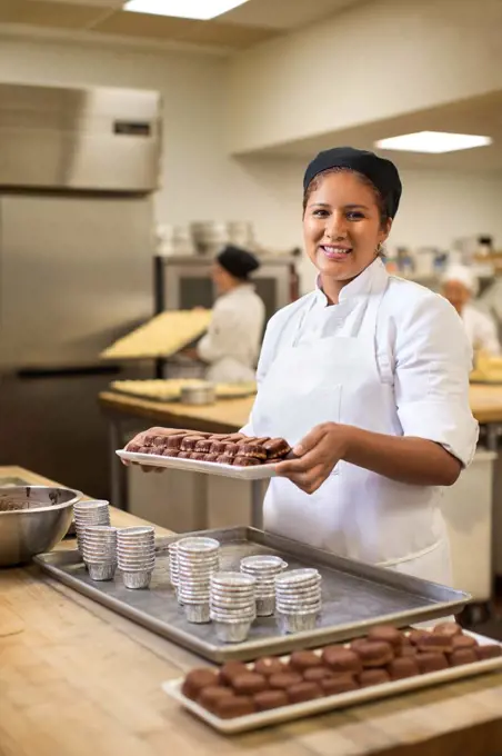 Portrait of female baker smiling in kitchen preparing individual sized sweet chocolate treats 