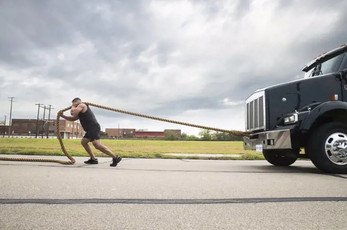 Muscular Hispanic man wearing tank top, Pulling semi truck with large tow rope 