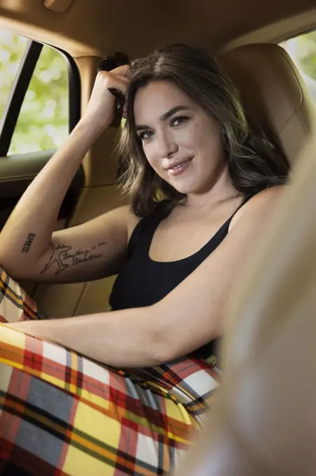 Portrait of caucasian casually dressed  woman with tattoos sitting in backseat of luxury sedan 