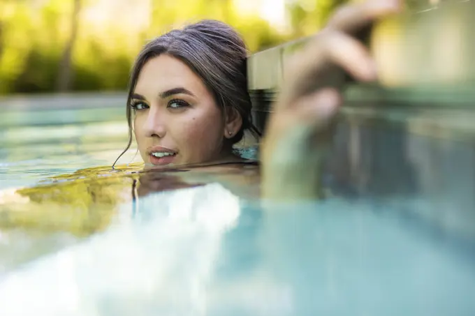 Portrait of caucasian woman floating in swimming pool in backyard looking at camera with a seductive expression.