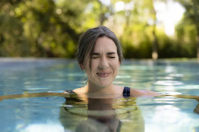 Portrait of caucasian woman floating in swimming pool in backyard making a squinting face.