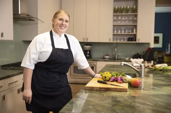 Portrait of Chef Megan Gill in kitchen looking up off camera, smiling.