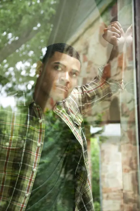 Portrait of a man in a plaid shirt standing at a window looking out thoughtfully.