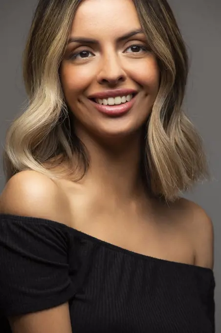 Happy beautiful young Hispanic woman looking off camera on gray background